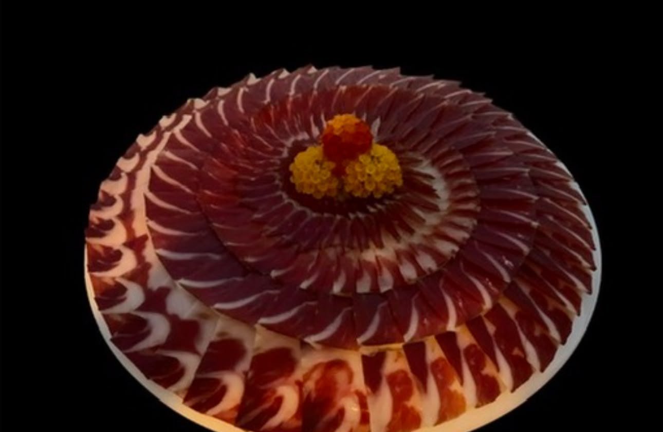 Presentación en espiral de lonchas de jamón ibérico con una flor comestible en el centro, vista desde arriba
