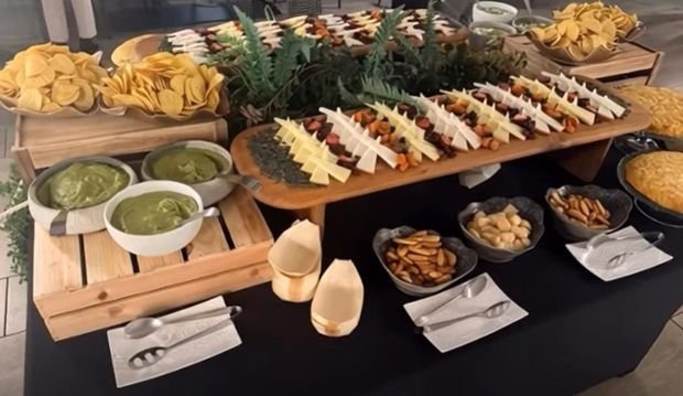 Mesa de catering gourmet con aperitivos, quesos y salsas sobre expositores de madera