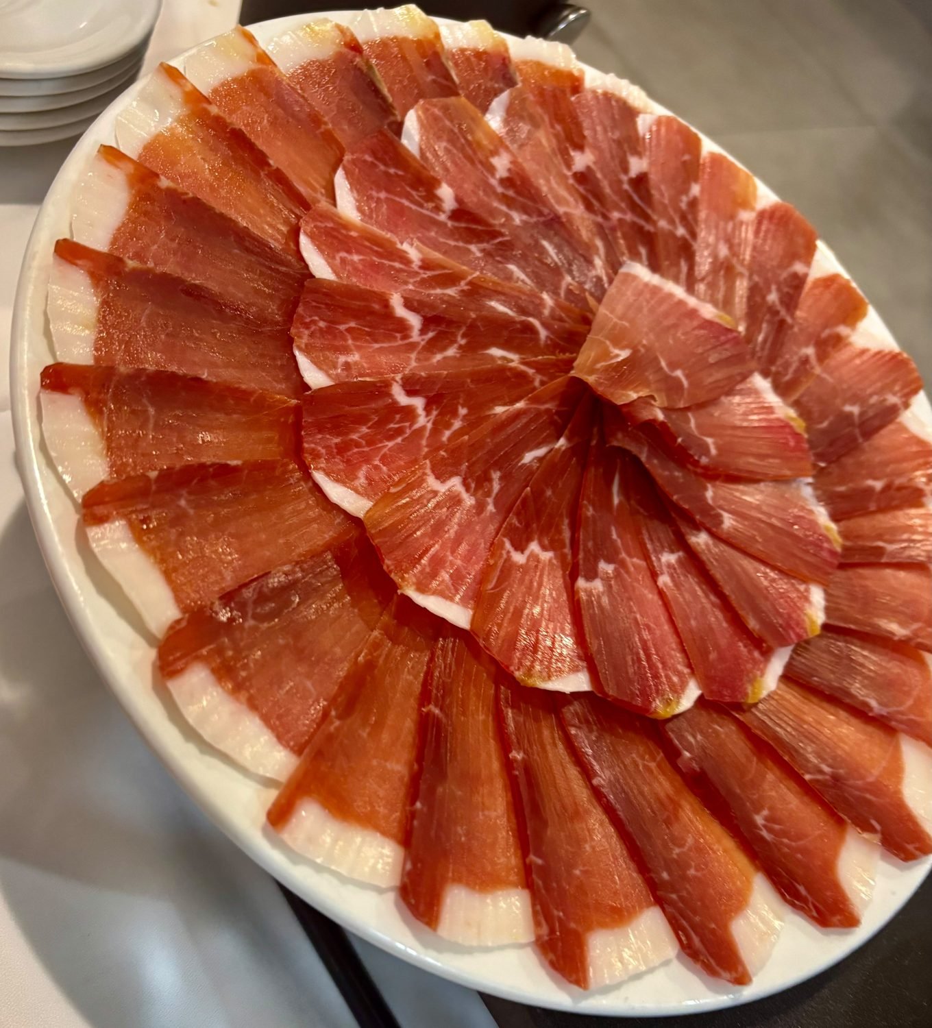 Fuente blanca con capas concéntricas de lonchas finas de jamón curado