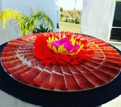Plato redondo de jamón en espiral decorado con una flor comestible en el centro