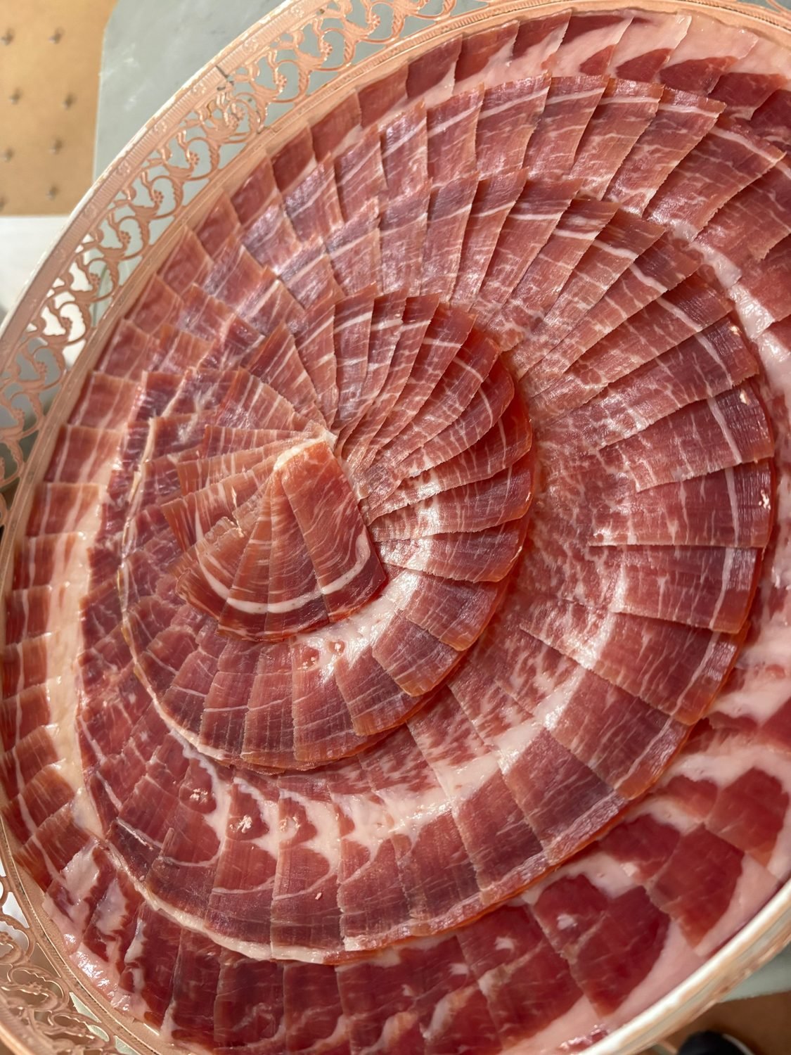 Vista cenital de lonchas de jamón en espiral sobre una bandeja decorativa