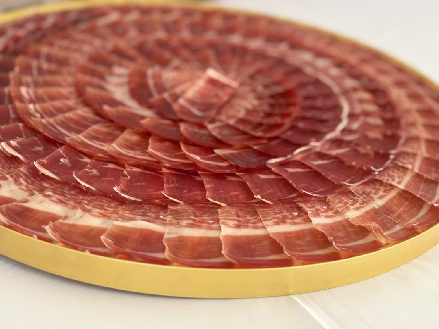 Detalle en ángulo de lonchas de jamón en capas circulares sobre bandeja dorada