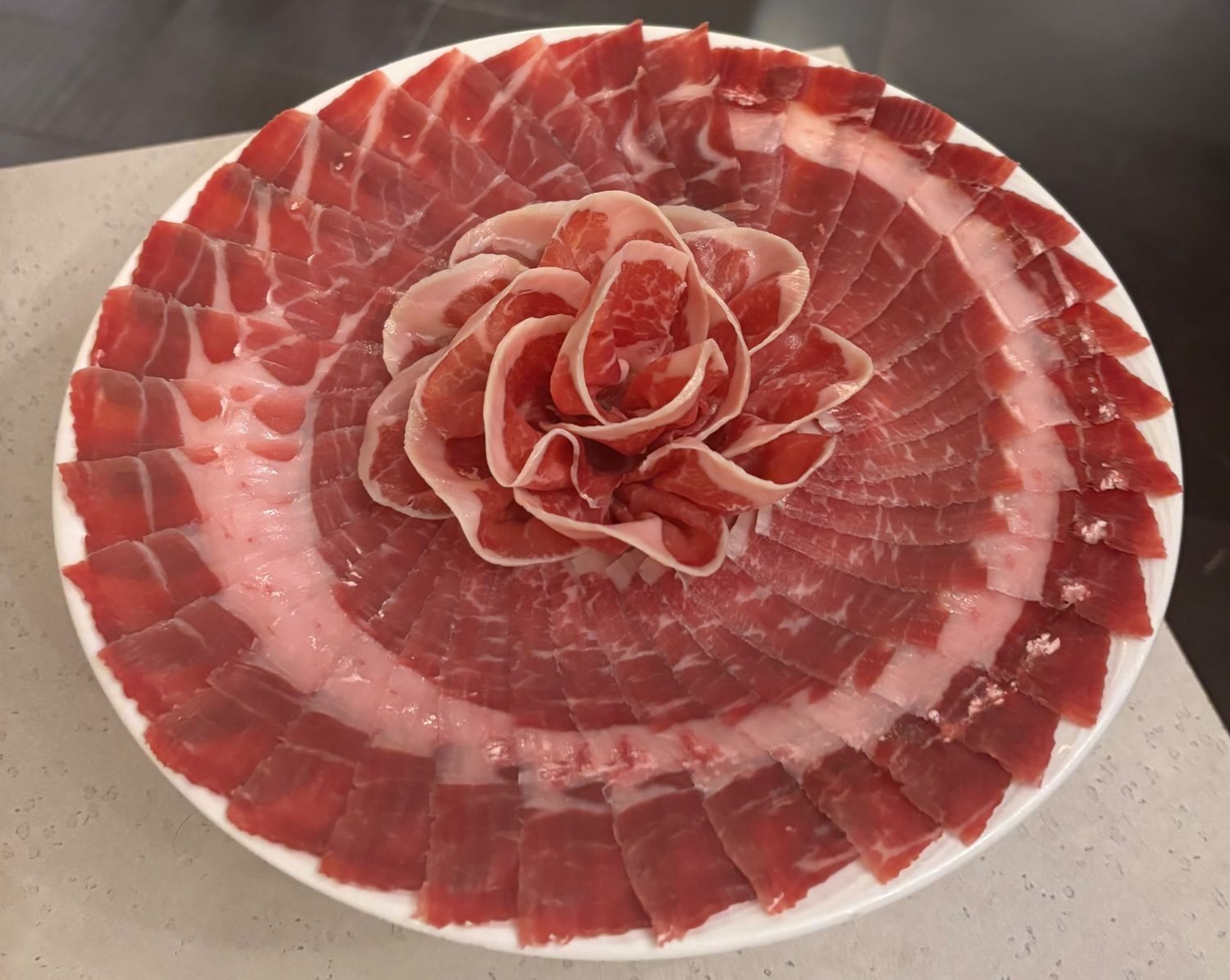 Plato redondo blanco con una rosa de lonchas de jamón en el centro