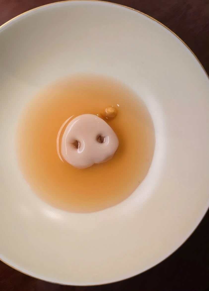 Consomé servido en cuenco blanco con un bocado de autor en el centro, aperitivo de un menú de evento