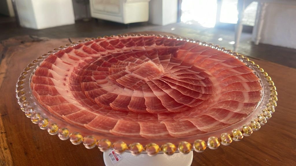 Plato de cristal con presentación en espiral de lonchas de jamón ibérico sobre mesa de madera, en interior